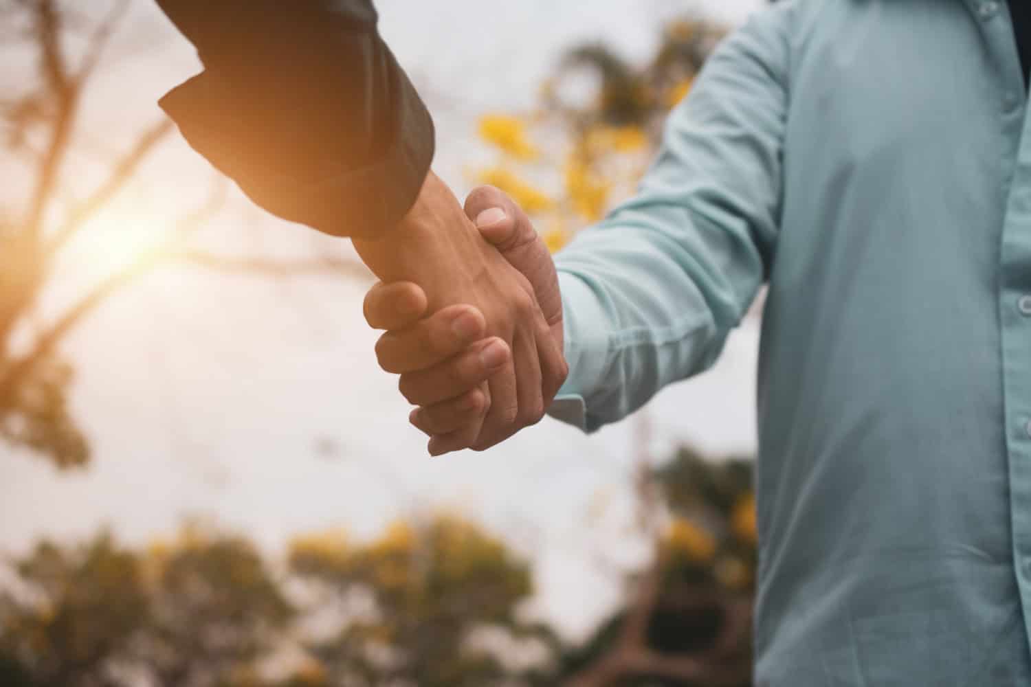 Atributos alt: Abrazo entre dos personas en un entorno al aire libre, simbolizando acuerdo y colaboración en un día soleado con árboles en el fondo.