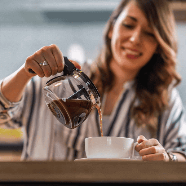 Taza de café siendo preparada con una cafetera por una mujer en un entorno luminoso y relajado.